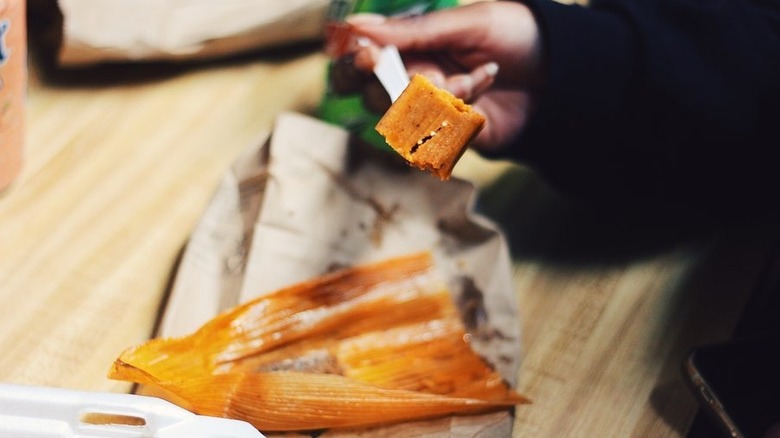 An unidentifiable person eating a tamale at Big Apple Inn