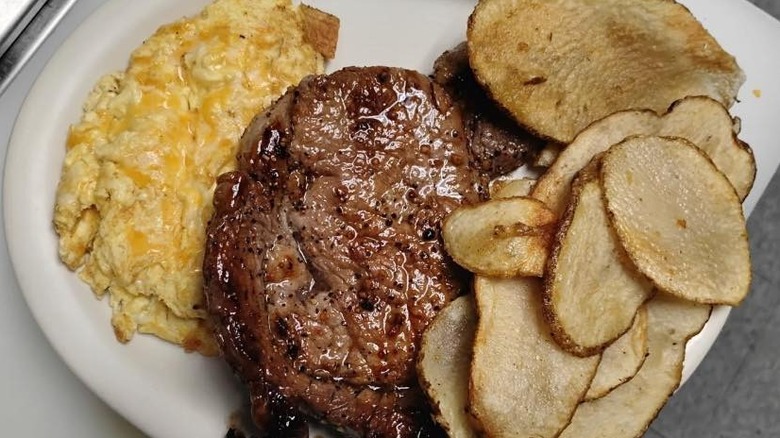 A plate of steak and cheesy eggs with thin sliced potatoes