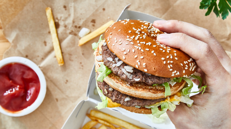 Hand holding takeout double decker hamburger