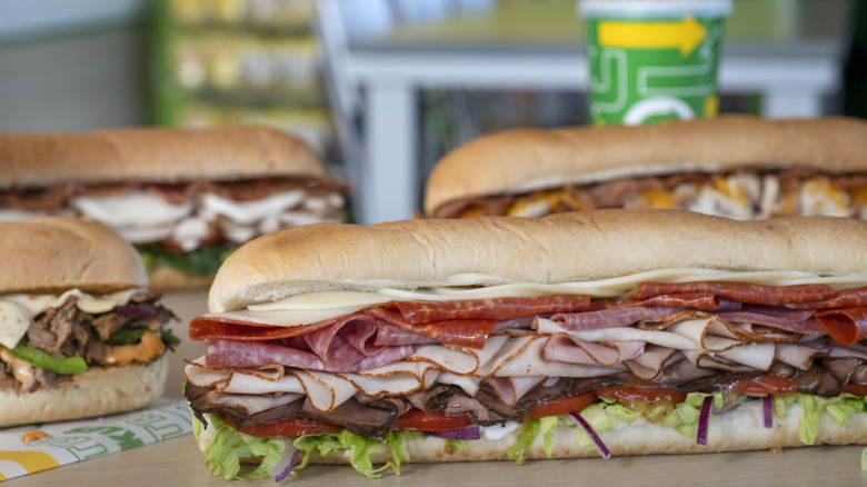 Subway sandwiches staggered behind each other with a Subway cup in the background
