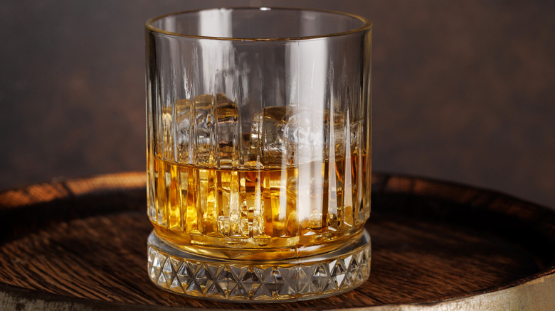 Glass of whisky on the rocks on top of barrel.