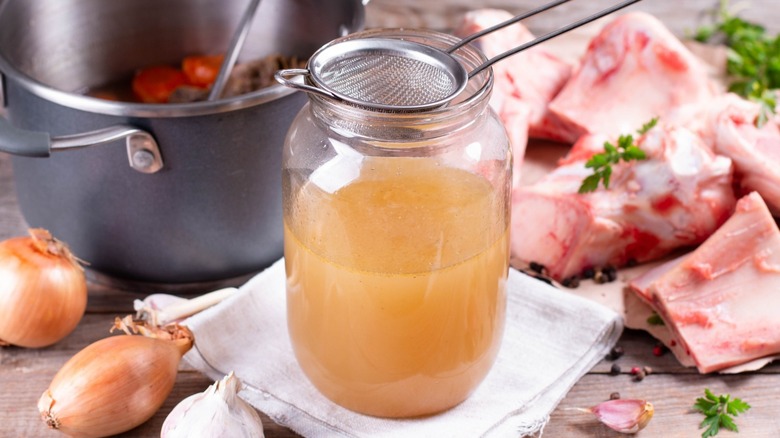 Person straining broth into glass jar