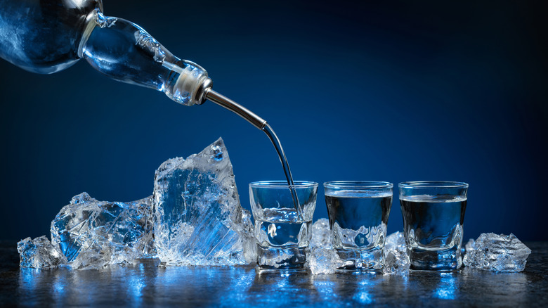 Shots of vodka being poured with ice in background