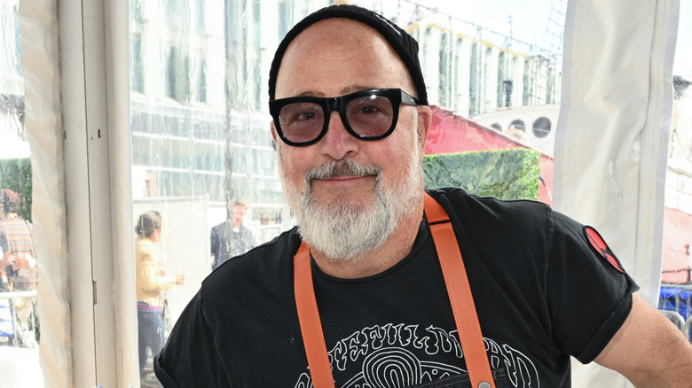 Andrew Zimmern wearing hat and sunglasses while smiling.