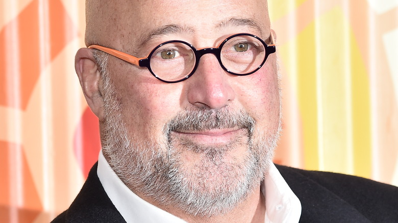 Andrew Zimmern wearing a black suit, white shirt and glasses