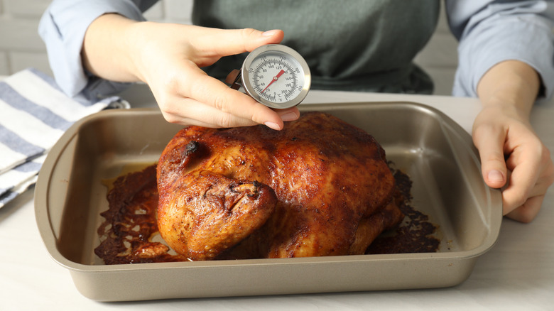 A hand placing a meat thermometer into the breast of a whole chicken