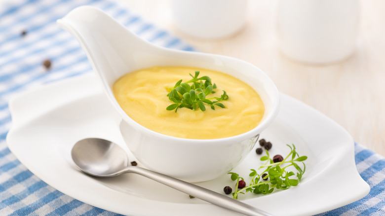 Hollandaise sauce in a white gravy boat on a blue napkin