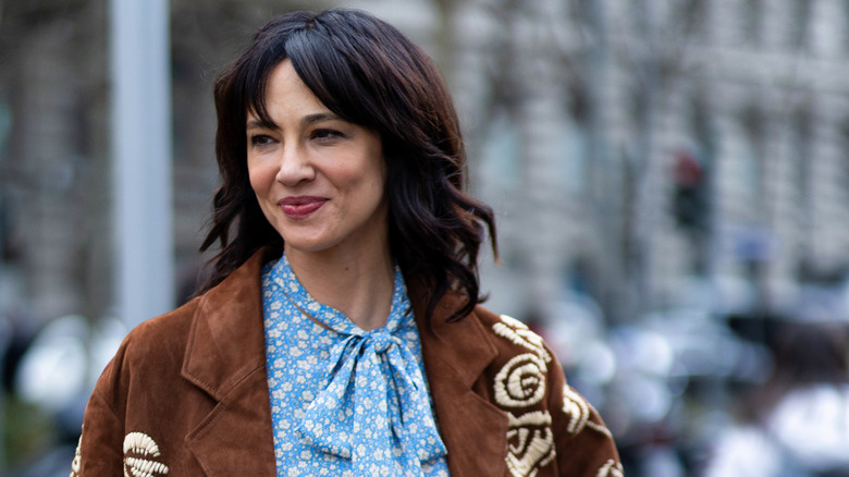 Asia Argento smiles in a brown suede jacket and a blue-and-white patterned shirt