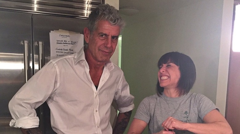 Anthony Bourdain stares at the camera while Ottavia Bourdain struggles to open a bottle of wine