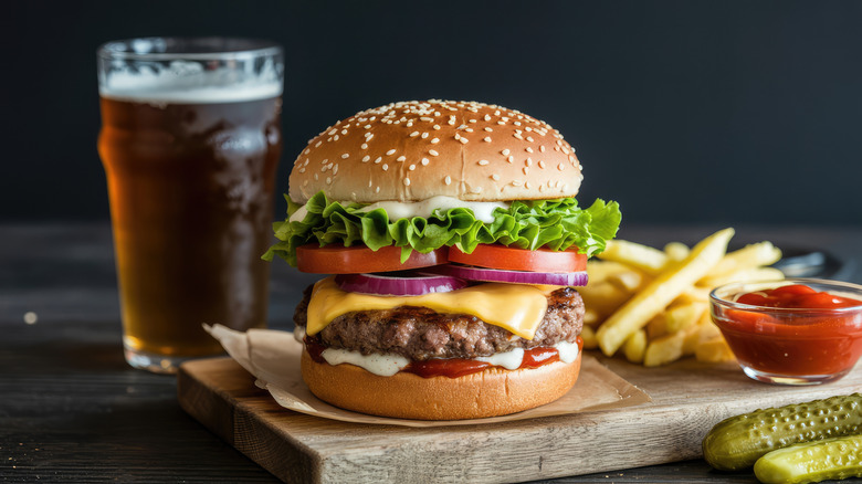 A hefty gourmet cheeseburger with red onions, tomato and lettuce next to a pint of beer and fries