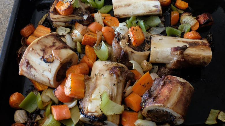 Oven roasted beef bones in a pan with carrots, onions, and celery.