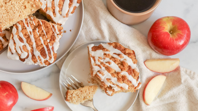 Apple crumb coffee cake slice on plate surrounded by more cake slices, whole apples, and apple slices