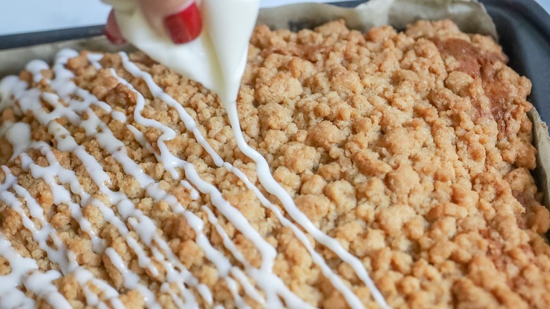 Icing drizzling on top of crumb-topped coffee cake