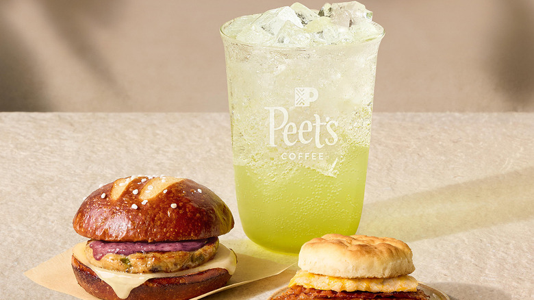 Peet's Coffee sparkling green apple energy drink with ice next to two sandwiches on a beige background