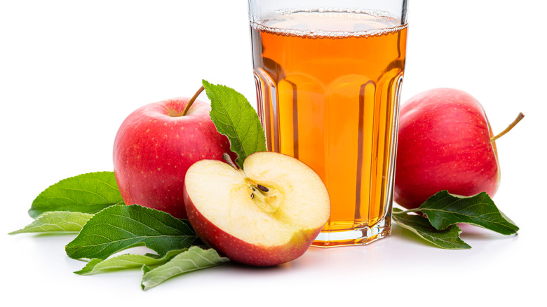 A glass of apple juice surrounded by apple halves.