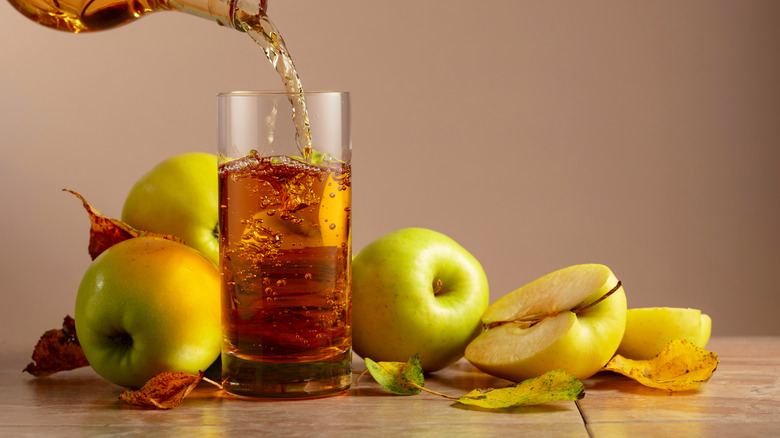 A glass of apple juice surrounded by apple halves.