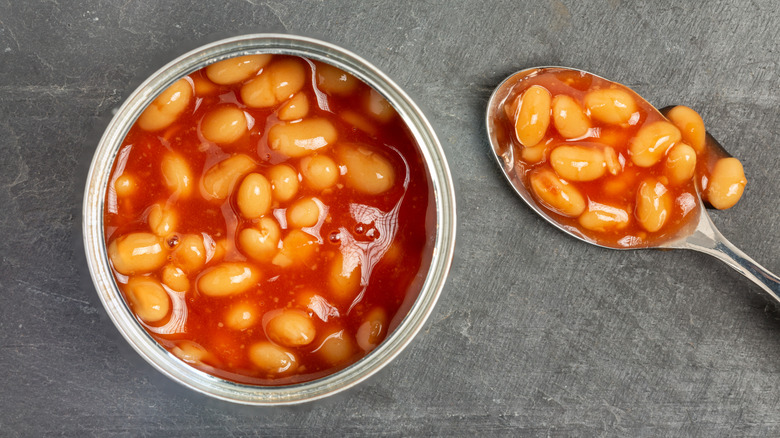 Top view of open can of baked beans and a beans-filled spoon next to it