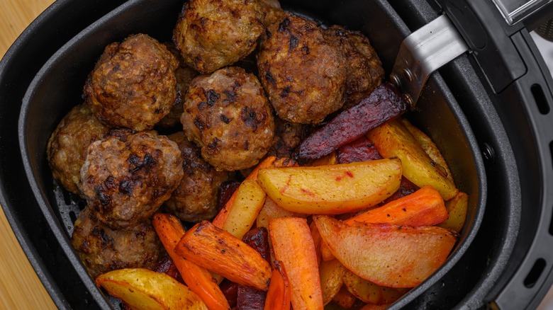 Baked meatballs and roasted vegetables in an air fryer basket.