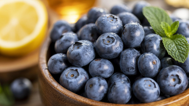 Close-up of blueberries in wooden bowl with mint leaves.