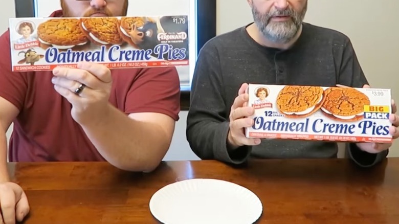 two men holding up Little Debbie oatmeal creme pie normal and big pack