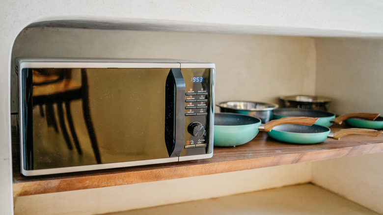 A sleek black and white microwave on a wooden counter near pots and pans
