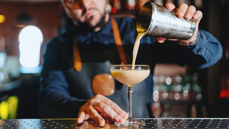Bartender pouring cocktail into clear stemware glass representing Absinth heavy-version of Aunt Roberta