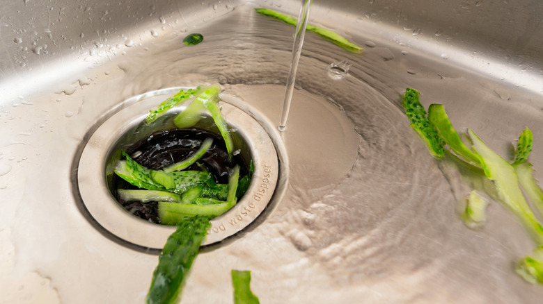 Green cucumber peels washed down a garbage disposal in a metal sink with water