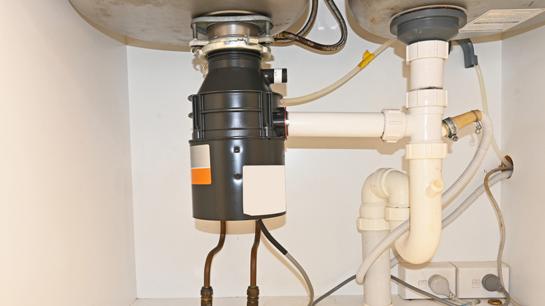 A black garbage disposal unit under a sink connected with pipes