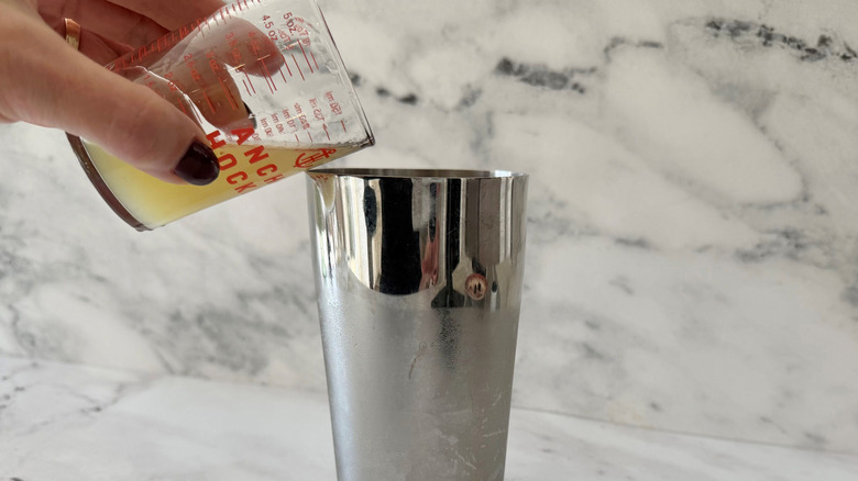 Hand pouring lemon juice into cocktail shaker