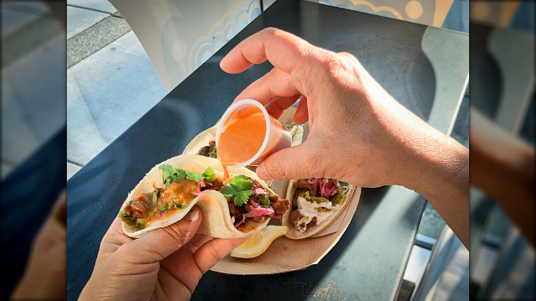 Person adding hot sauce to a taco