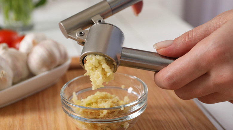 Person using garlic press with garlic in bowl