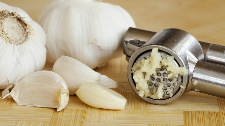 Garlic press alongside peeled and unpeeled cloves