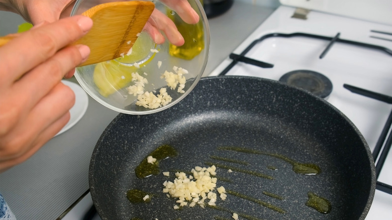 Hands adding chopped garlic to pan