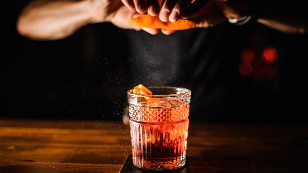 bartender squeezing an orange peel over the glass