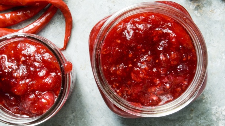 Two jars of chili jam with hot chilis in the background