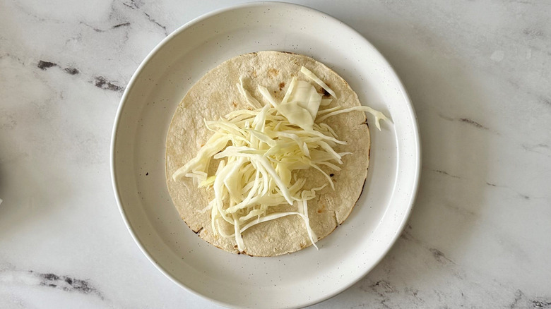 Cabbage on top of tortilla on plate
