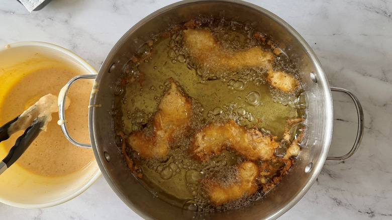 Battered fish frying in pot of oil