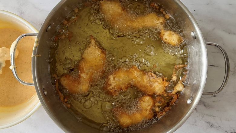 Battered fish frying in pot of oil