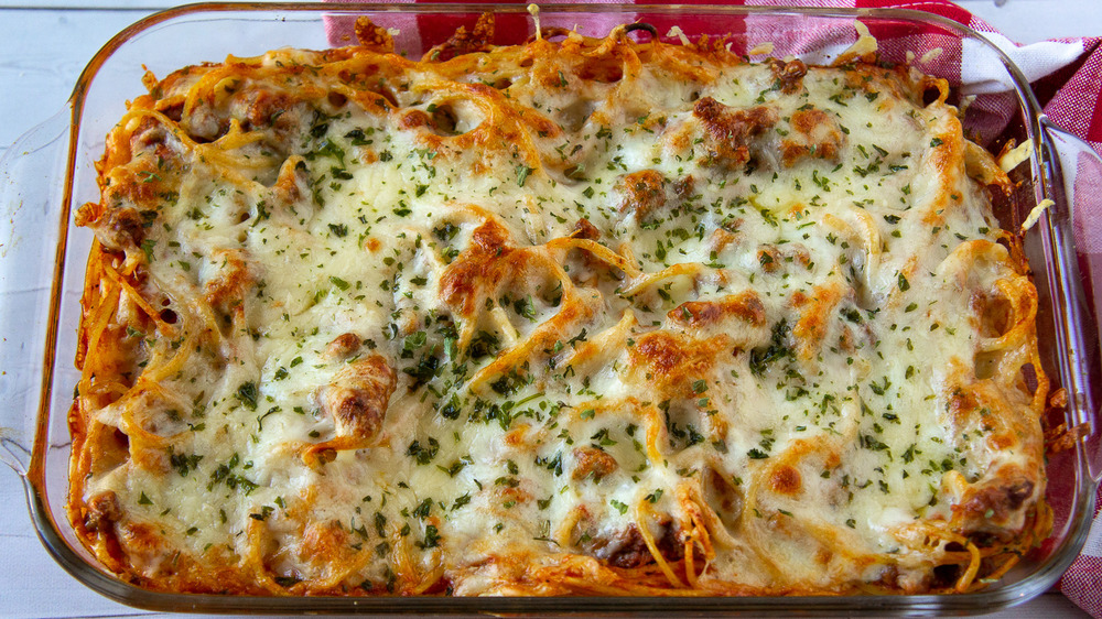 A glass baking dish with baked spaghetti next to a red checked towel