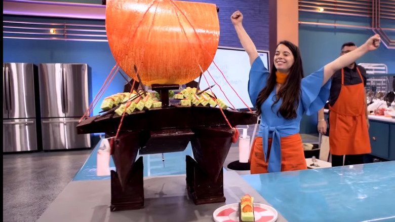 Baking Impossible contestant raising arms