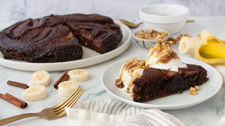 Slice of bananas foster brownie on plate with ice cream with larger brownie in background