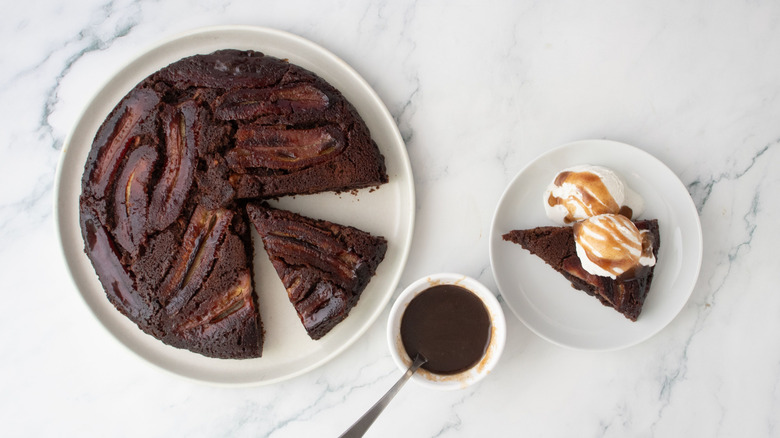 Bananas Foster brownie with slices removed next to bowl of sauce and slice with ice cream and drizzle of sauce on plate