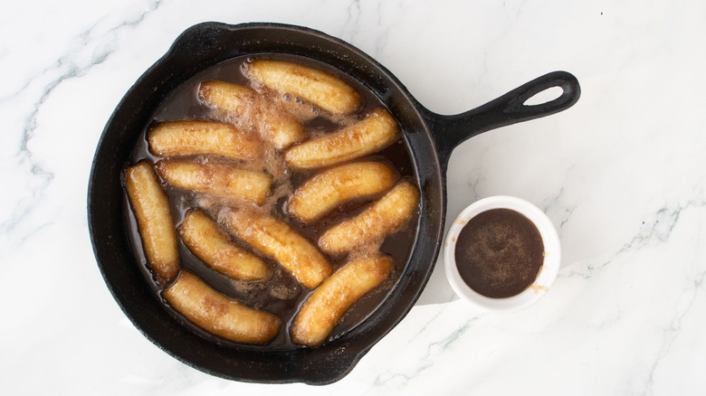 Bananas Foster in skillet next to small bowl of sauce