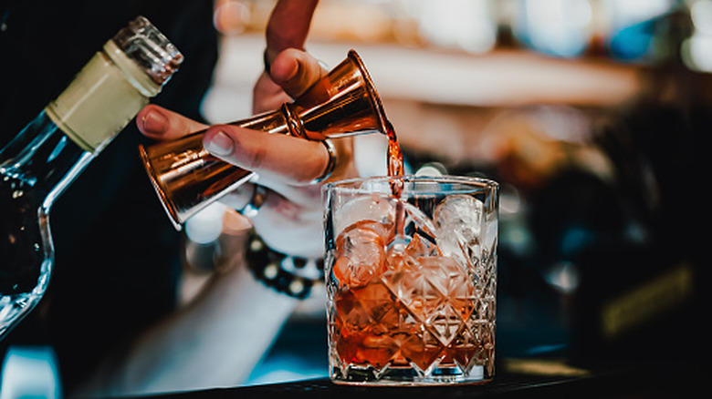 Bartender pouring liquor from jigger into rocks glass