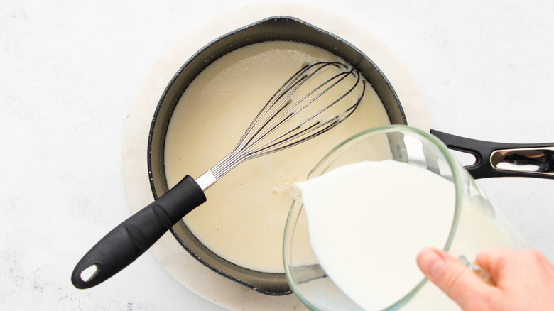 Pouring milk into saucepan with whisk