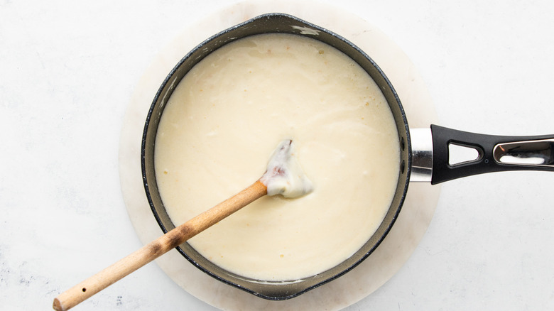 Cheese sauce in saucepan with wooden spoon