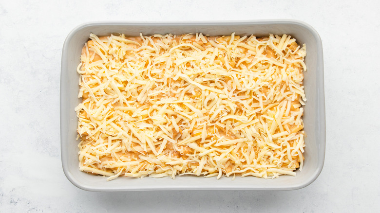 Mac and cheese mixture in baking dish, topped with shredded cheese
