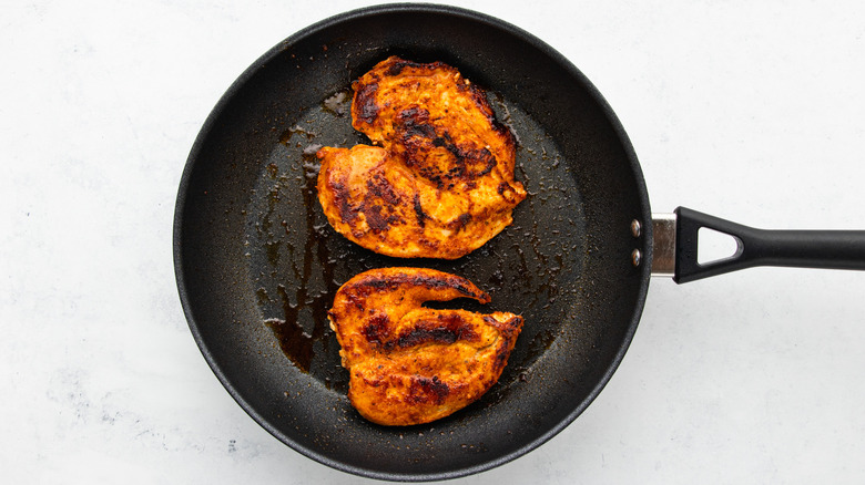 Spice-covered, butterflied chicken breasts cooking in frying pan