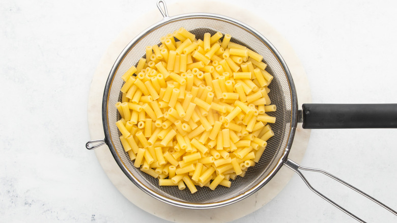 Cooked macaroni pasta in strainer over saucepan