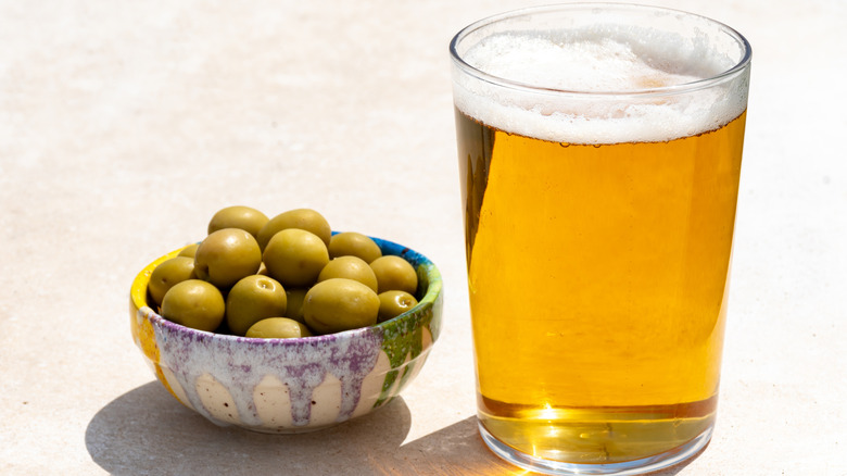 A glass of beer next to a bowl of green olives